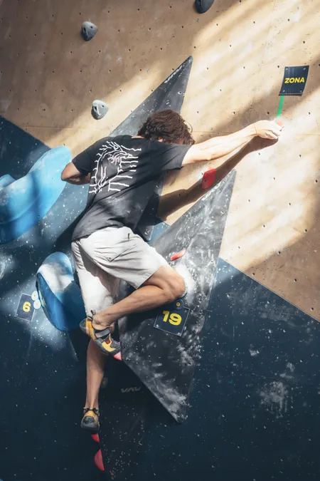 A climber mid-move on a steep bouldering wall at a competition.